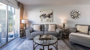 A modern living room with a grey sofa set, a glass coffee table, and a large abstract painting on the wall.