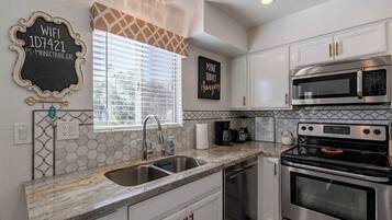 A modern kitchen with white cabinets, stainless steel appliances, a granite countertop, and a window with blinds.