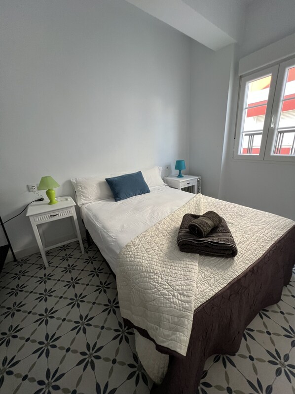 A bedroom with a bed, two bedside tables, a window, and patterned floor tiles. - Charming House in the Center of Ayamonte (Ayamonte)