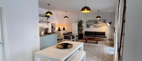 A spacious living area with a white table and bench, patterned floor tiles, and pendant lighting.