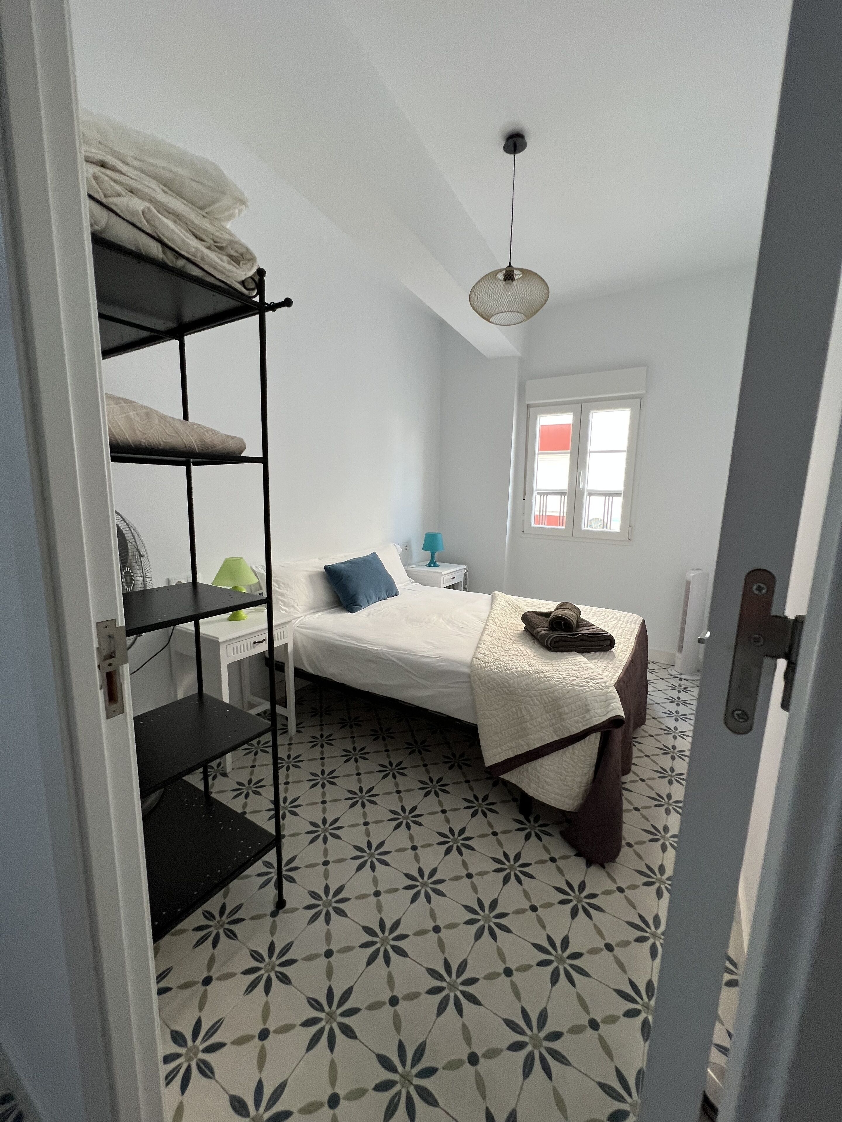 Une chambre à coucher de taille réduite, comprenant un lit, une petite table de chevet, une lampe et une fenêtre.