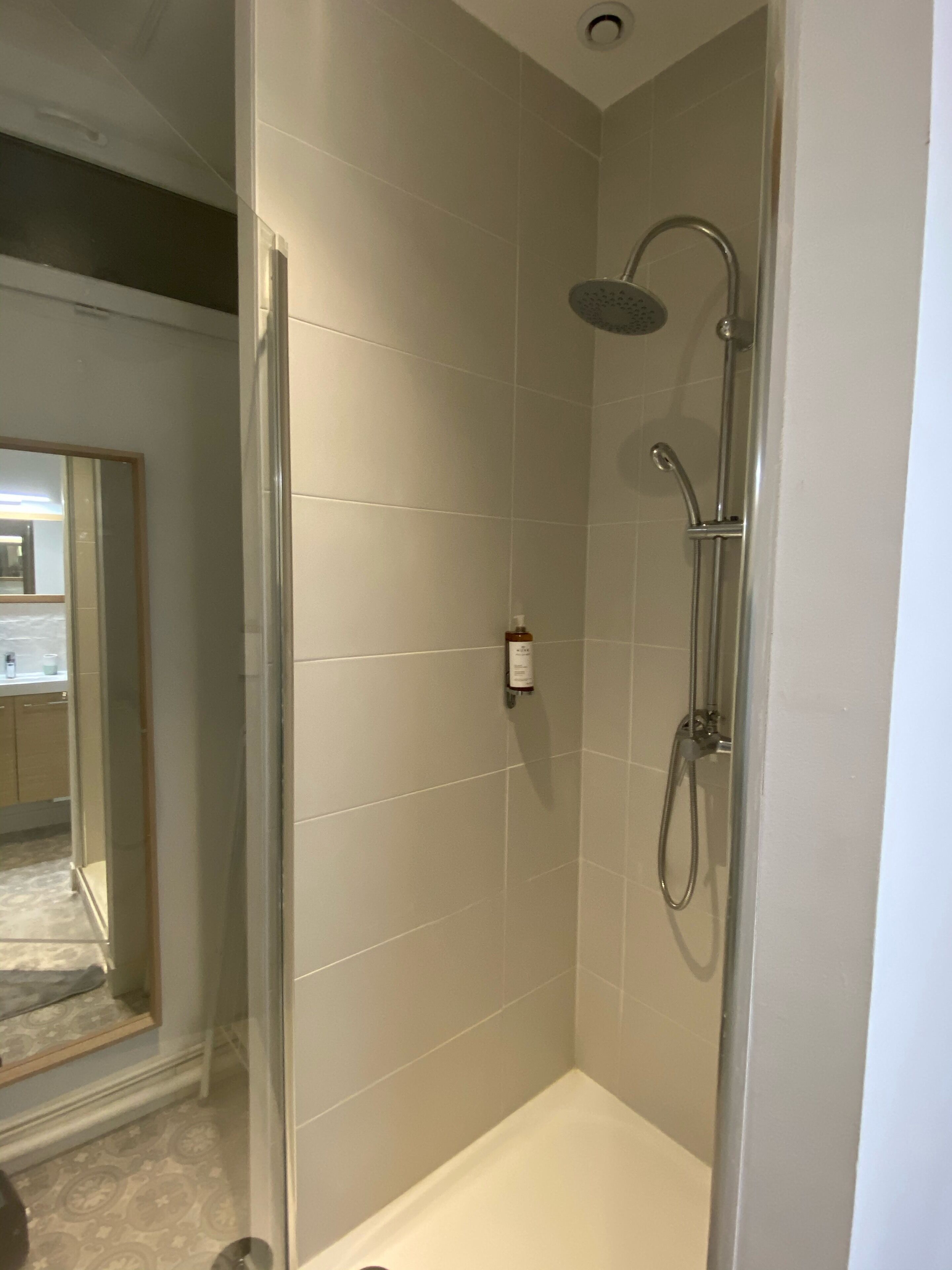 Un petit espace douche fermé, équipé d’un pommeau de douche à main et d’un robinet à main.