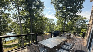 Eine Holzterrasse mit Tisch und Stühlen mit Blick auf einen See, umgeben von Bäumen.