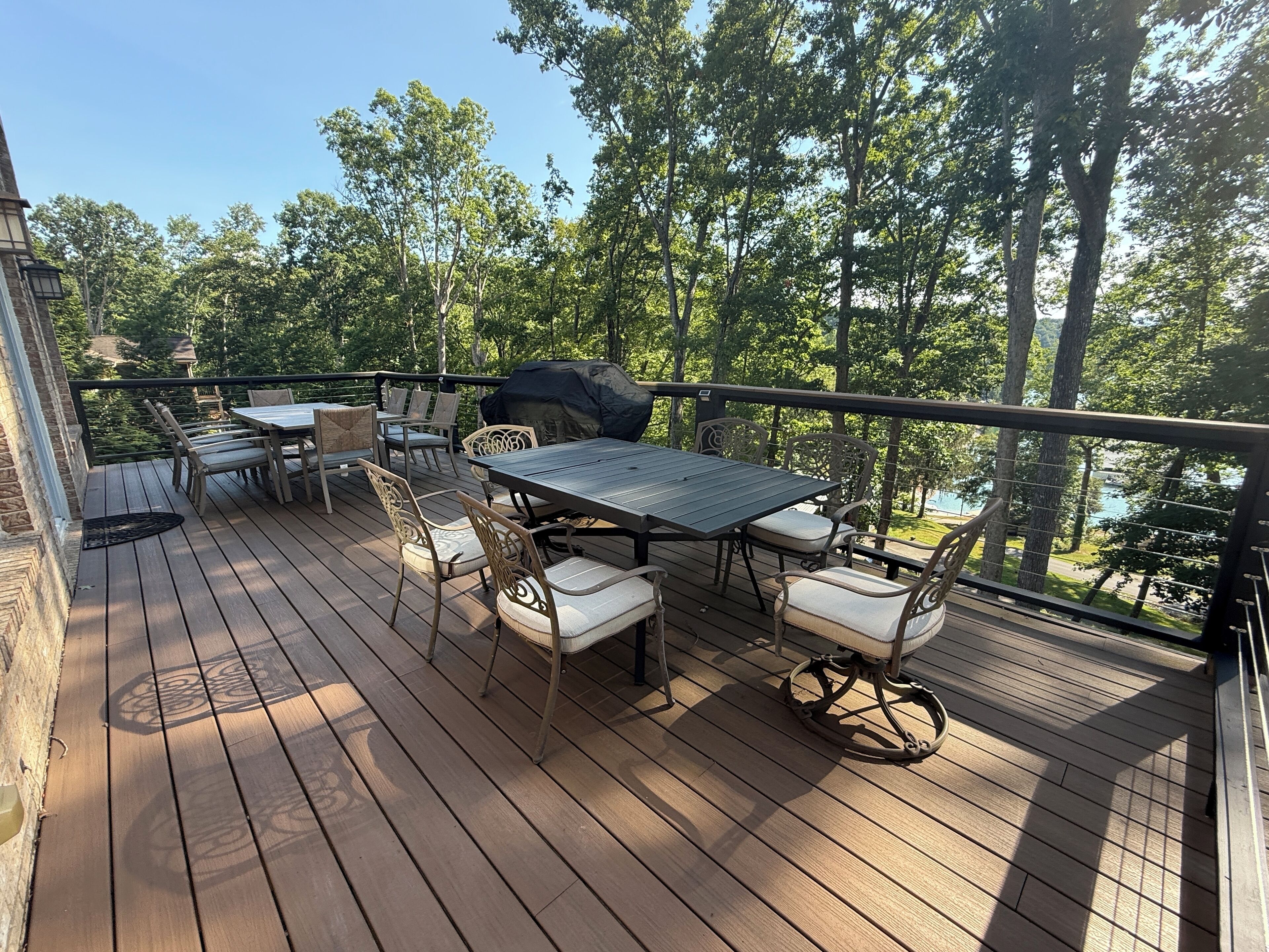 A wooden deck with a table and chairs, surrounded by trees and a view of a body of water.