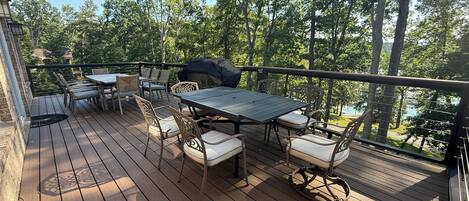 A wooden deck with a table and chairs, surrounded by trees and a view of a body of water.