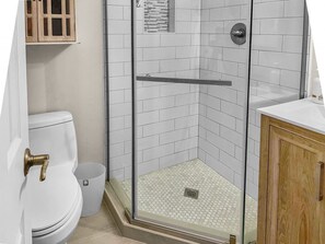 Ein Badezimmer mit einer Duschkabine aus Glas, einer Toilette und einem Holzschrank.