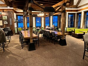 A restaurant with wooden beams, large windows, and multiple tables and chairs.