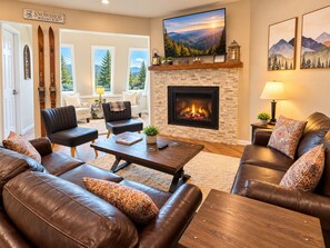 Una sala de estar acogedora con chimenea, sofás de cuero, una mesa de centro y un televisor sobre la chimenea.