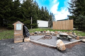 Un área con fogones, una estructura de madera con el letrero "Fire Pit Rules" y una caravana blanca estacionada cerca.