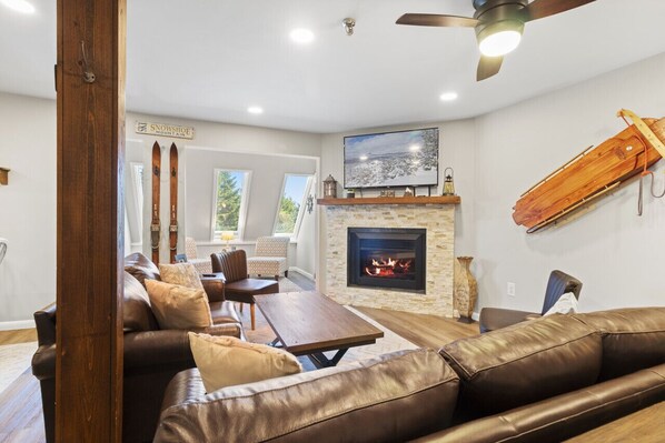 A cozy living room with a fireplace, leather sofas, a wooden coffee table, and a mounted television.