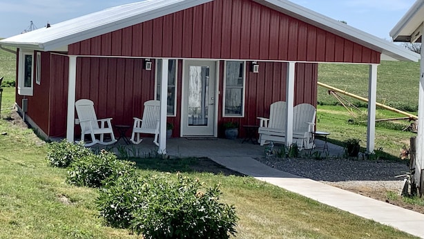 A red barn with a covered porch, white chairs, and a small table. - Little Country House a Quiet Countryside Getaway! (Newton)