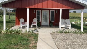 A red building with a porch, two white chairs, a small table, and a potted plant. - Little Country House a Quiet Countryside Getaway! (Newton)