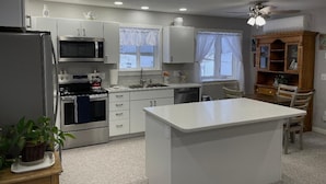 A modern kitchen with white cabinetry, a built-in microwave, a stove, and a large island. - Little Country House a Quiet Countryside Getaway! (Newton)