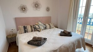 Un dormitorio con cama, mesita de noche, decoración en la pared y vistas a través de una ventana.