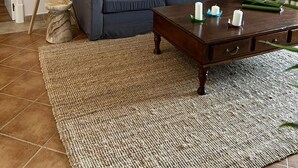 Una sala de estar con un sofá azul oscuro, una mesa de centro de madera con velas, un tapete tejido y una lámpara.