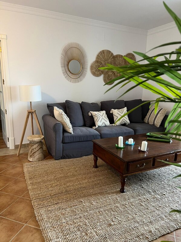 A living room with a dark blue sofa, a wooden coffee table with candles, a woven rug, and a lamp.