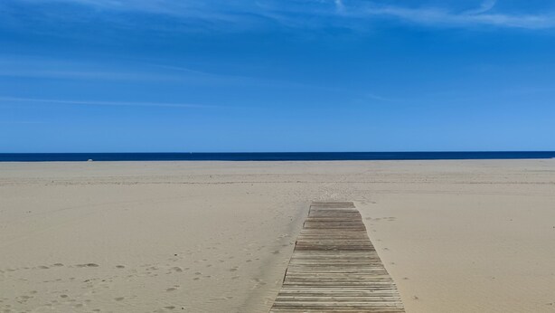 Una extensa playa de arena con un paseo marítimo de madera que conduce al agua.