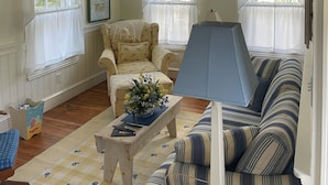 A cozy living room with a wooden ceiling, a striped sofa, a chair, and a table with a vase.