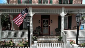 A two-story house with a porch, a white picket fence, and an American flag.