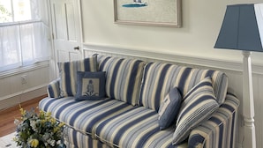 A room with a striped sofa, a framed beach painting, and a lamp.