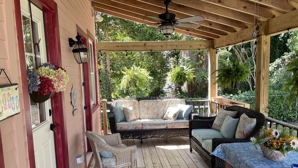 A covered porch with a wooden ceiling, a ceiling fan, and a sofa with patterned cushions.