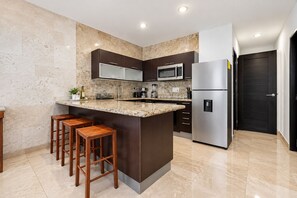 A modern kitchen with a marble countertop, stainless steel appliances, and wooden stools.