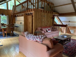 A cozy cabin interior with a wooden dining area, a sofa with patterned cushions, and a staircase leading to an upper level.