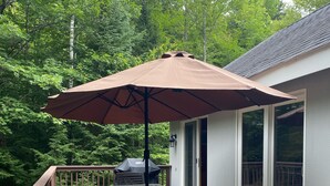 A wooden deck with a table and chairs, a large umbrella, and a grill. - White Mountain Retreat, Waterville Estates Amenities  (Campton)