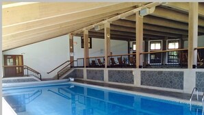 An indoor swimming pool with clear water, a wooden deck, and a stone wall. - White Mountain Retreat, Waterville Estates Amenities  (Campton)