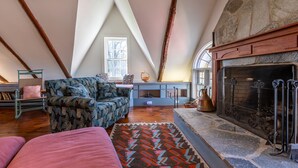 A cozy loft bedroom with exposed wooden beams, a stone fireplace, a patterned rug, and a comfortable seating area. - Beautiful Historic Country Estate – Modern Comfort in Okemo Valley (Cavendish)