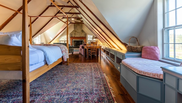 A cozy attic bedroom with a sloped ceiling, a wooden bed, a small table, and a window with a view. - Beautiful Historic Country Estate – Modern Comfort in Okemo Valley (Cavendish)