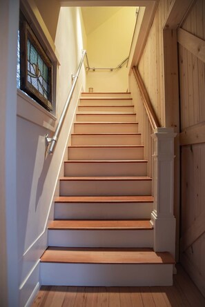 Een houten trap met witte leuningen en een handrail, die uitkomt op een uitloop met een glazen deur.