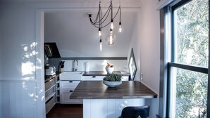 A modern kitchen with a wooden island, pendant lighting, and a view of trees through a large window.