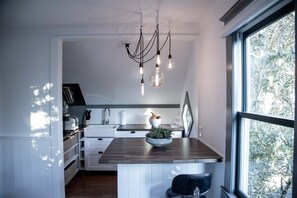 Een moderne keuken met een houten keukeneiland, hanglampen en uitzicht op bomen door een groot raam.
