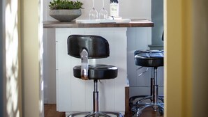 A modern kitchen with a white countertop, two bar stools, a hanging light fixture, and a wine bottle.
