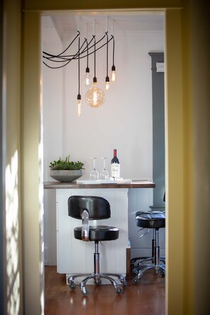 Een moderne keuken met een wit aanrecht, twee barkrukken, een hanglamp en een fles wijn.