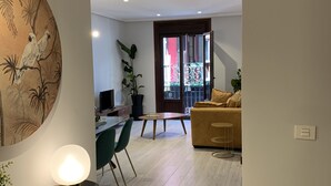 A modern living room with a yellow sofa, a dining area with a round table and chairs, and a large wall mural.