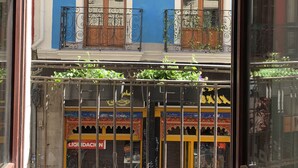 A view through a window of a building with a blue facade, balconies with wrought iron railings, and a storefront with colorful signage.