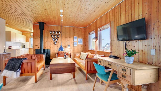 A cozy cabin-style room with a wooden interior, a fireplace, a dining table, and a TV mounted on the wall. - Gorgeous home in Harboøre with WiFi (Harboøre)