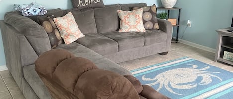 Un salón con un amplio sofá modular, un sillón reclinable marrón, un adorno de pared y una lámpara de pie.