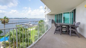 A balcony with a view of the water, a table with chairs, and a pool in the background. - Luxurious Caribe bay-view condo, 4BR/3BA, sleeps 9 (Orange Beach)