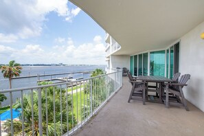 A balcony with a view of the water, a table with chairs, and a pool in the background. - Luxurious Caribe bay-view condo, 4BR/3BA, sleeps 9 (Orange Beach)