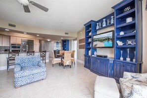 A spacious living area with a dining table, chairs, a sofa, and a built-in entertainment unit with decorative items. - Cozy Nautical Condo Overlooking Perdido Bay! Complimentary Boat Slip! (Orange Beach)
