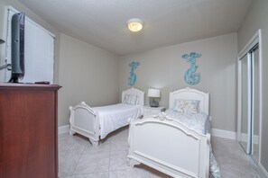 Un dormitorio con dos camas blancas, un aparador de madera, una lámpara de techo y decoración mural.