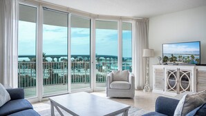 A spacious living room with a large sliding glass door leading to a balcony, a comfortable sofa, a coffee table, and a television on a cabinet.