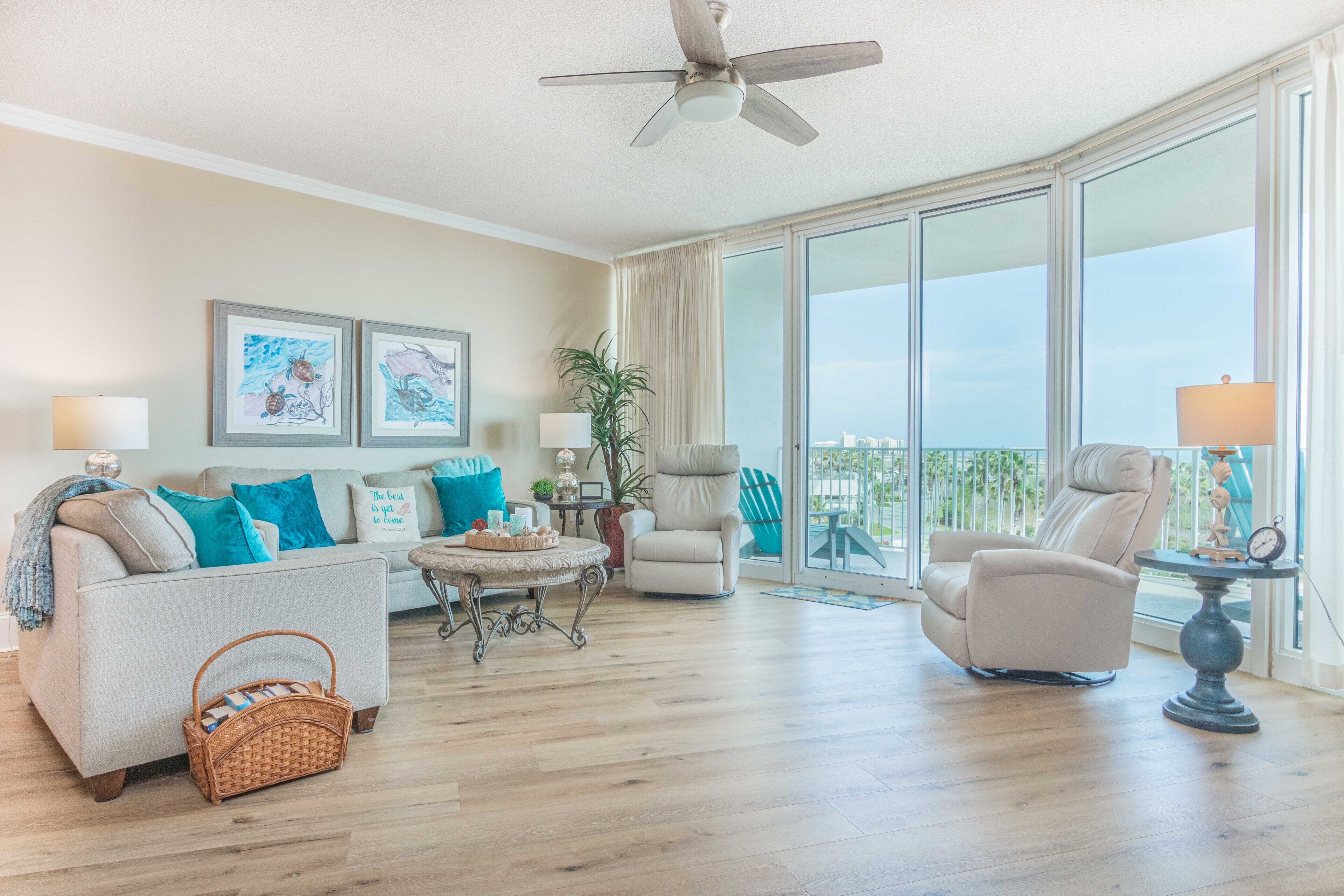A spacious living room with a large window, a ceiling fan, and a view of the city.