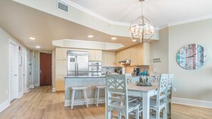 Una cocina moderna con una isla central, armarios de madera y un comedor con sillas blancas.