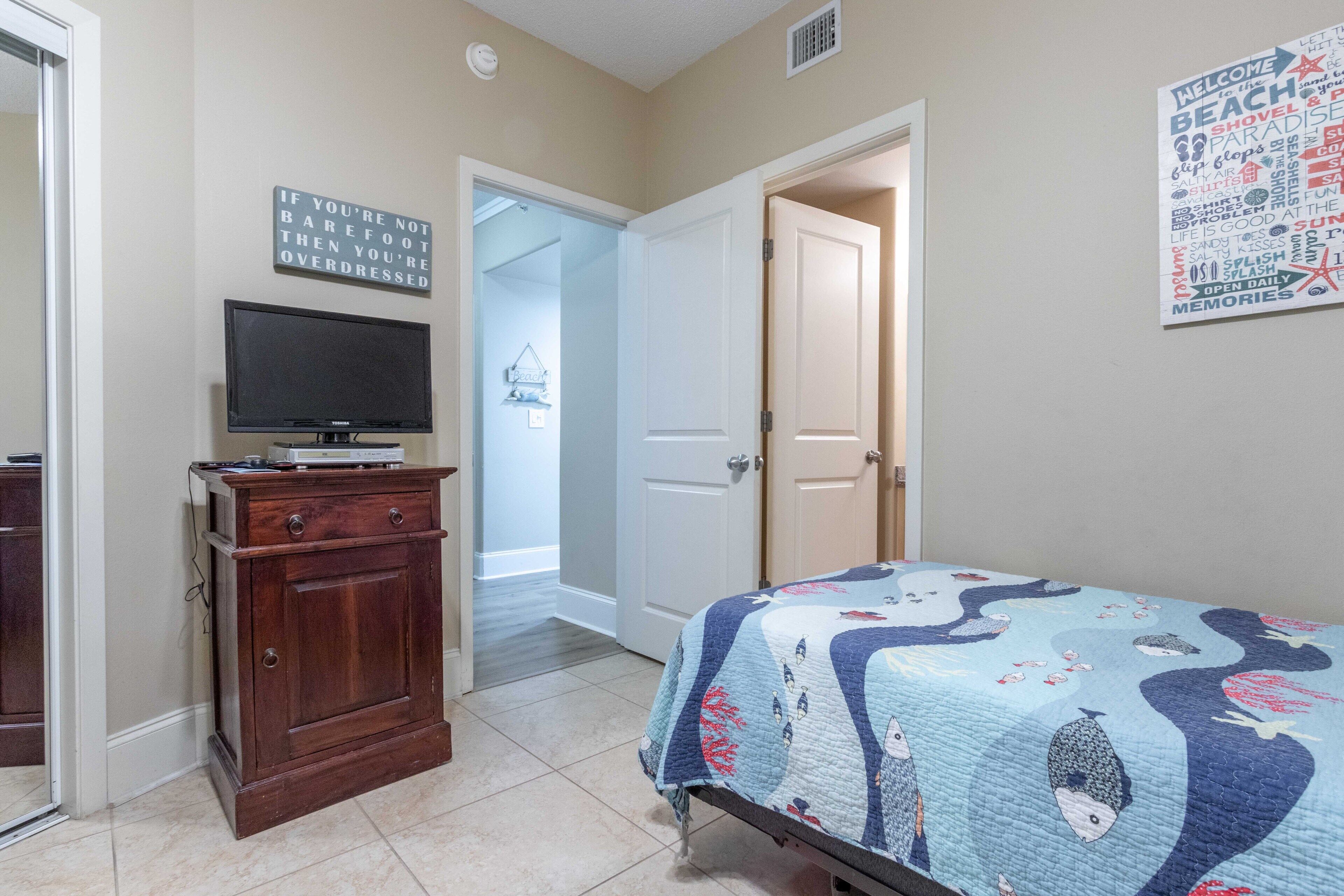Un dormitorio con cama, cómoda, televisor y puerta que da a otra habitación.