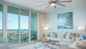 A spacious living room with a large sliding glass door leading to a balcony, a ceiling fan, a coffee table, and a sofa with decorative pillows. - Spacious Two Bedroom Condo with Bay and Gulf B609 Views! Complimentary Boat Slip! (Orange Beach)