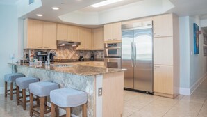 A modern kitchen with a central island, stainless steel appliances, and wooden cabinetry. - Spacious Two Bedroom Condo with Bay and Gulf B609 Views! Complimentary Boat Slip! (Orange Beach)